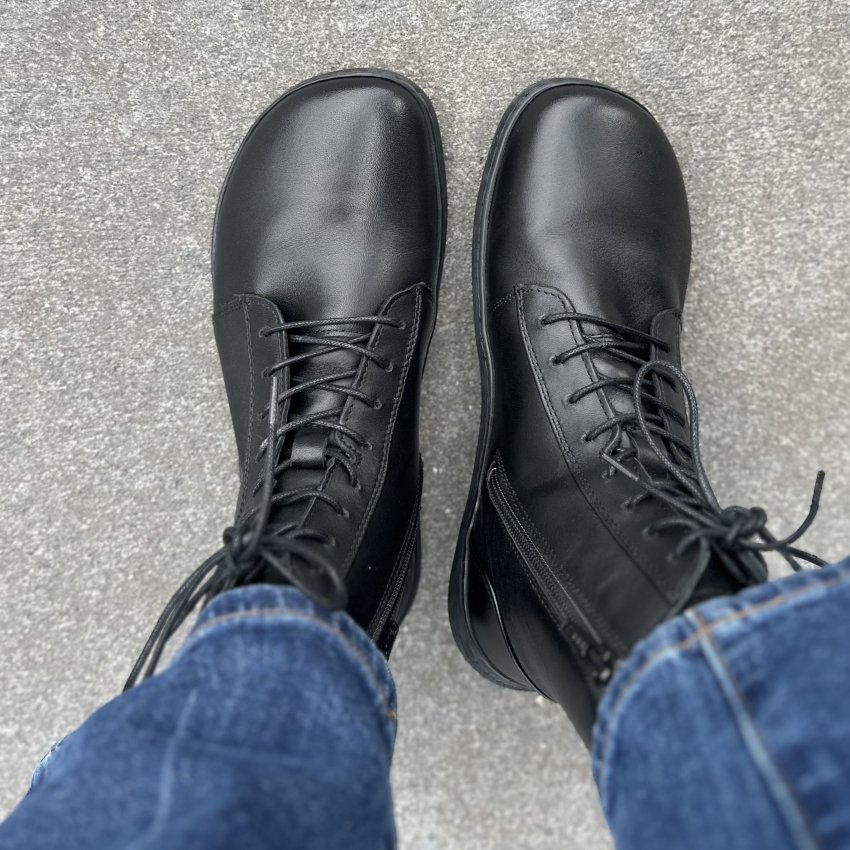 Top down view of a person's feet in black leather lace up boots with a side zipper from Skinners. The wide toe box black boots are being worn with jeans and the wide toe box is prominently shown.