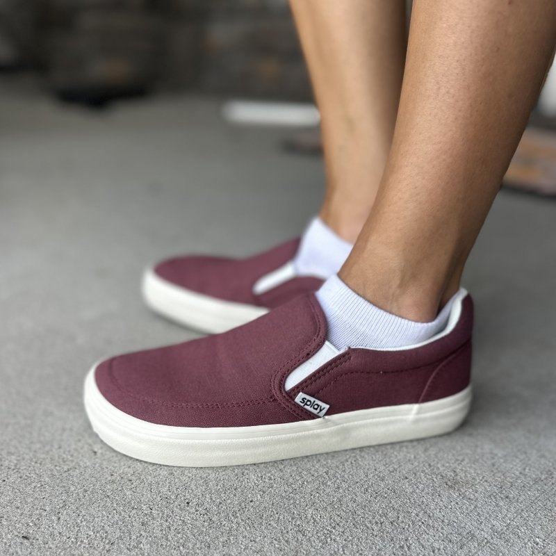A side view of a person wearing maroon canvas Splay Rev SO slip-on barefoot sneakers with a wide toe box