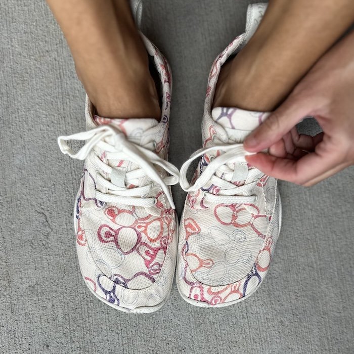A top down view of a pair of feet resting on concrete wearing the Wildling Shoes Tanuki Asawa printed barefoot shoes