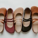 A collection shot of 4 colors of Jenon Leather Villet Double Strap Mary Janes with a wide toe box. They are all lined up alternating toe box directions and are shown in colors brown, burgundy, beige, and black.