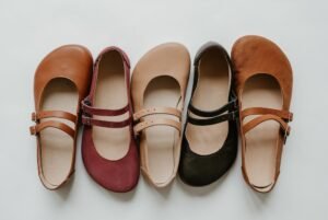 A collection shot of 4 colors of Jenon Leather Villet Double Strap Mary Janes with a wide toe box. They are all lined up alternating toe box directions and are shown in colors brown, burgundy, beige, and black.