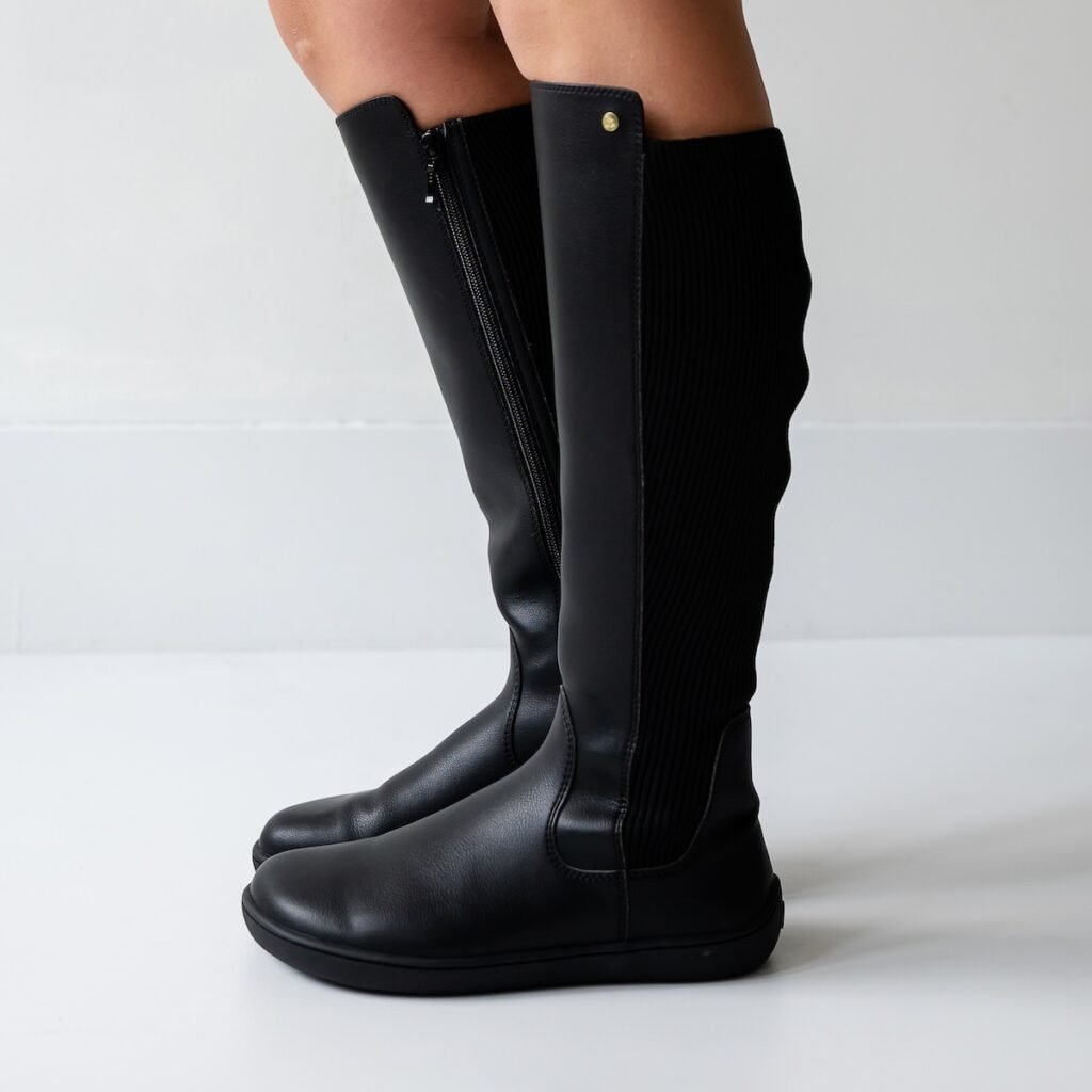 A close up side view of a woman's legs from the knee down wearing black leather Be Lenka Symphony tall barefoot riding boots