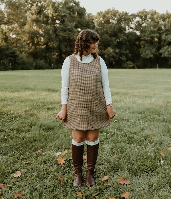 A woman standing in a field of grass looking to the side wearing a plaid mini dress and knee high brown leather Shapen Glam barefoot riding boots