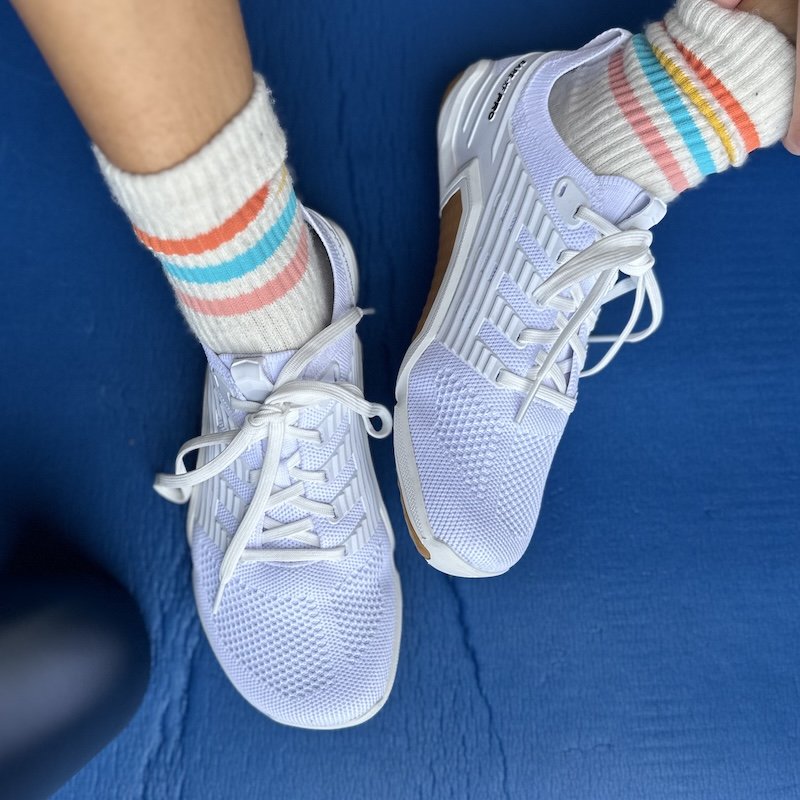 A top down view of a pair of feet resting on an exercise mat wearing striped socks and white Inov8 Bare XF cross training gym shoes