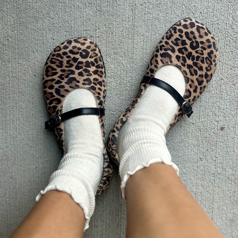 Top down view of a pair of leopard mary jane ballerinas from Lang S, with a black strap. The wide toe box flats are being worn with a pair of ruffle crew socks.
