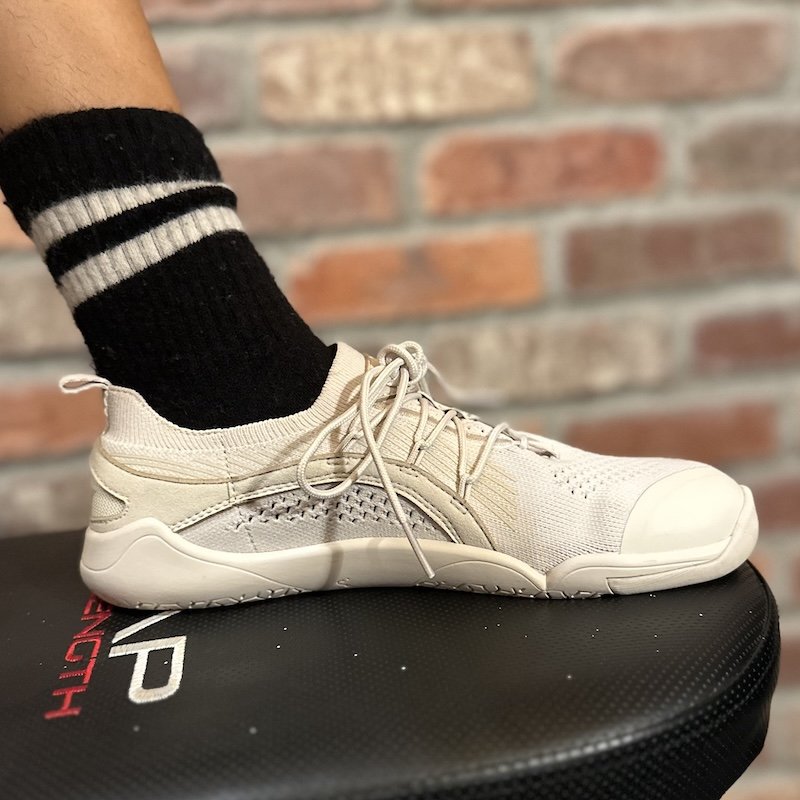 A close up side view of a foot resting on an exercise bench wearing a black sock and Lono Wear Flow 2 barefoot trainers