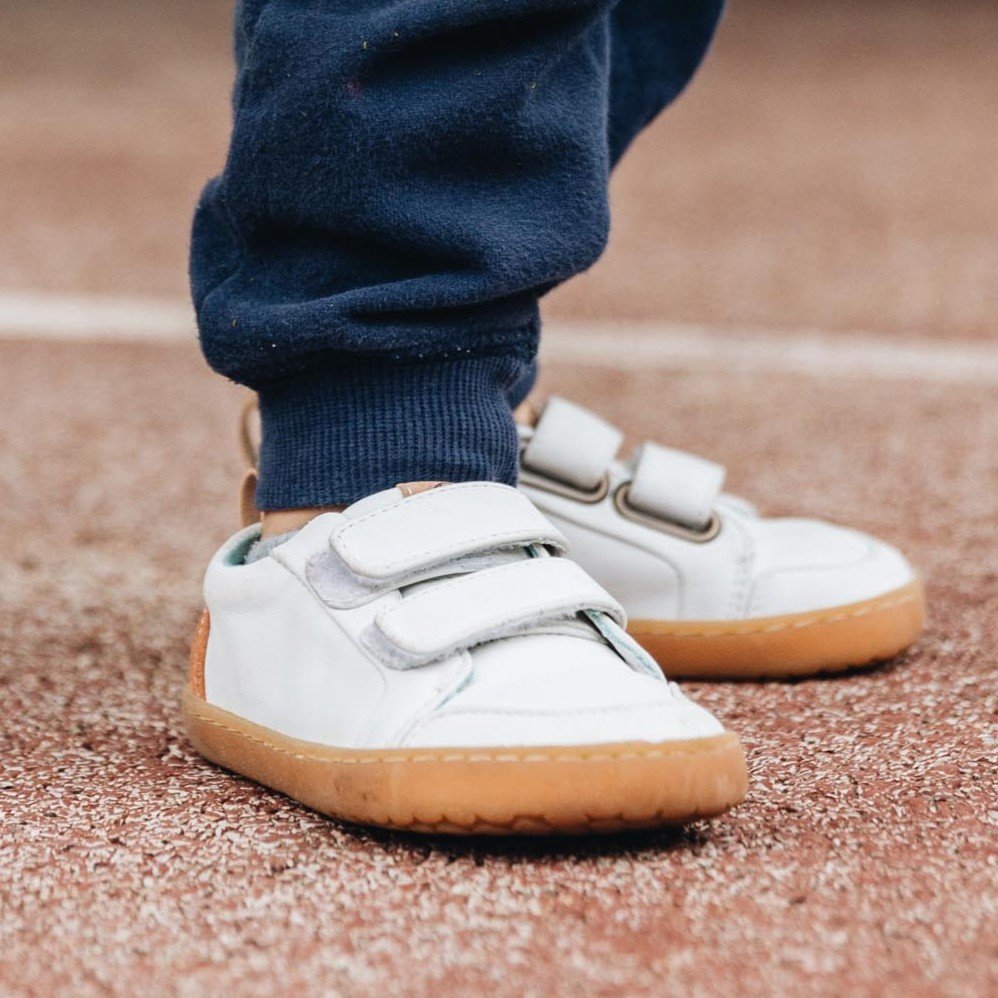 Front side close up of a little child's feet in Mukishoes Nimbus white leather barefoot sneakers for play.