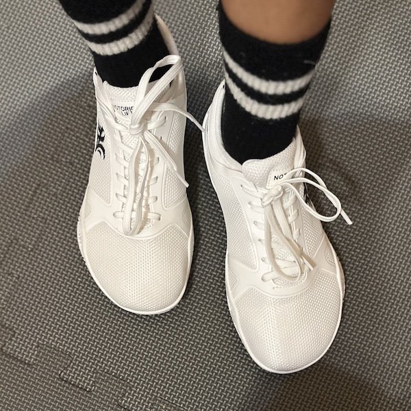 A top down view of a pair of feet wearing black stocks and white Notorious Lift Radix Pro lifting shoes with a wide toe box