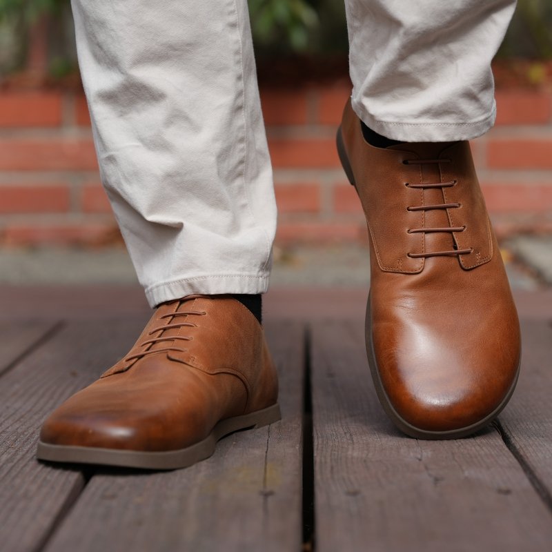 Front view of a man's feet in Oaka Jefferson leather wide toe box dress shoes. The foot on the right is picked up and the left is flat on the ground. A pair of khaki pants are resting at the ankle.