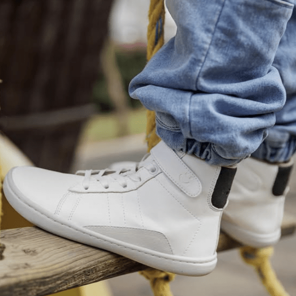 A kid wearing a pair of Origo High tops in white leather on a wooden swing