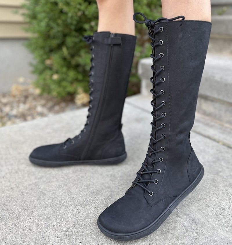 A close up of a woman's lefts wearing knee high lace up barefoot boots in black leather - the Koel Flora