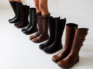 A line up 6 different barefoot knee high boots in black and brown lined up in a row
