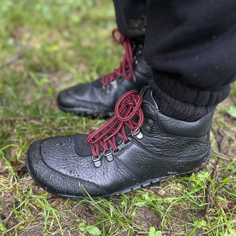 Side profile view of a pair of Baer Mountain Hiking Boots with a wide toe box and flat outsole for stability. They are black leather with classic red laces.