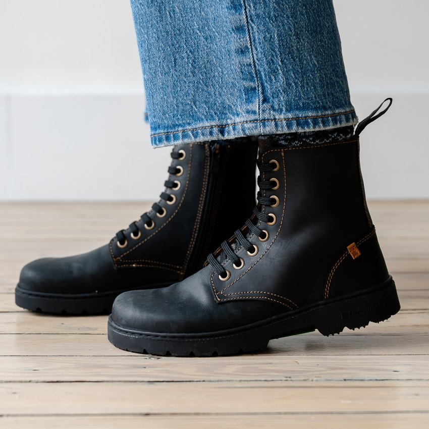 Side close up of a person's feet in black leather El Naturalista Nomada lace up minimalist boots with flexible outsole. The side view shows the front foot flexed up.