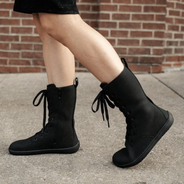 A side view of a person walking in a pair of Be Lenka Evon barefoot combat style boots with a side zip.