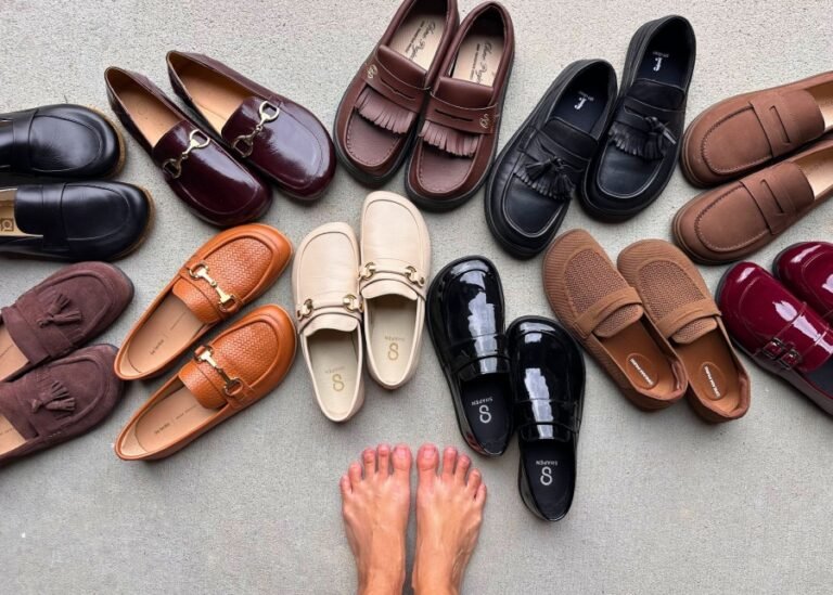 A person's feet standing bare in front of a spread of multiple barefoot loafers with a wide toe box