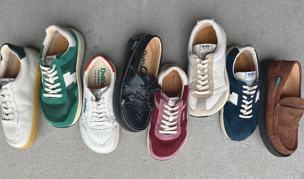 A row of different wide toe box Dolfie Paradise barefoot sneakers and shoes laid out on concrete in different colors and models.
