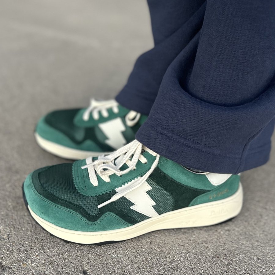 Side view of a person's feet in navy athletic pants and a pair of Dolfie Paradise supersonic chunky anatomical sneakers in emerald green with a white bolt on the side.
