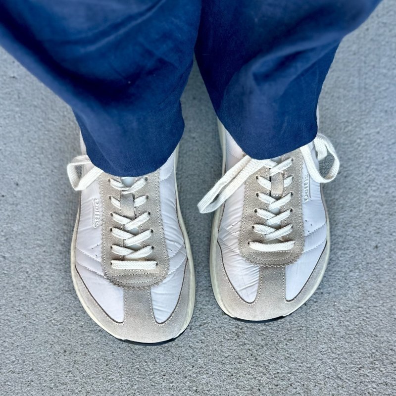 Top down view of a person's feet in navy linen pants and a pair of Dolfie Paradise white and gray chunky Supersonic sneakers with a comfortable wide toe box.