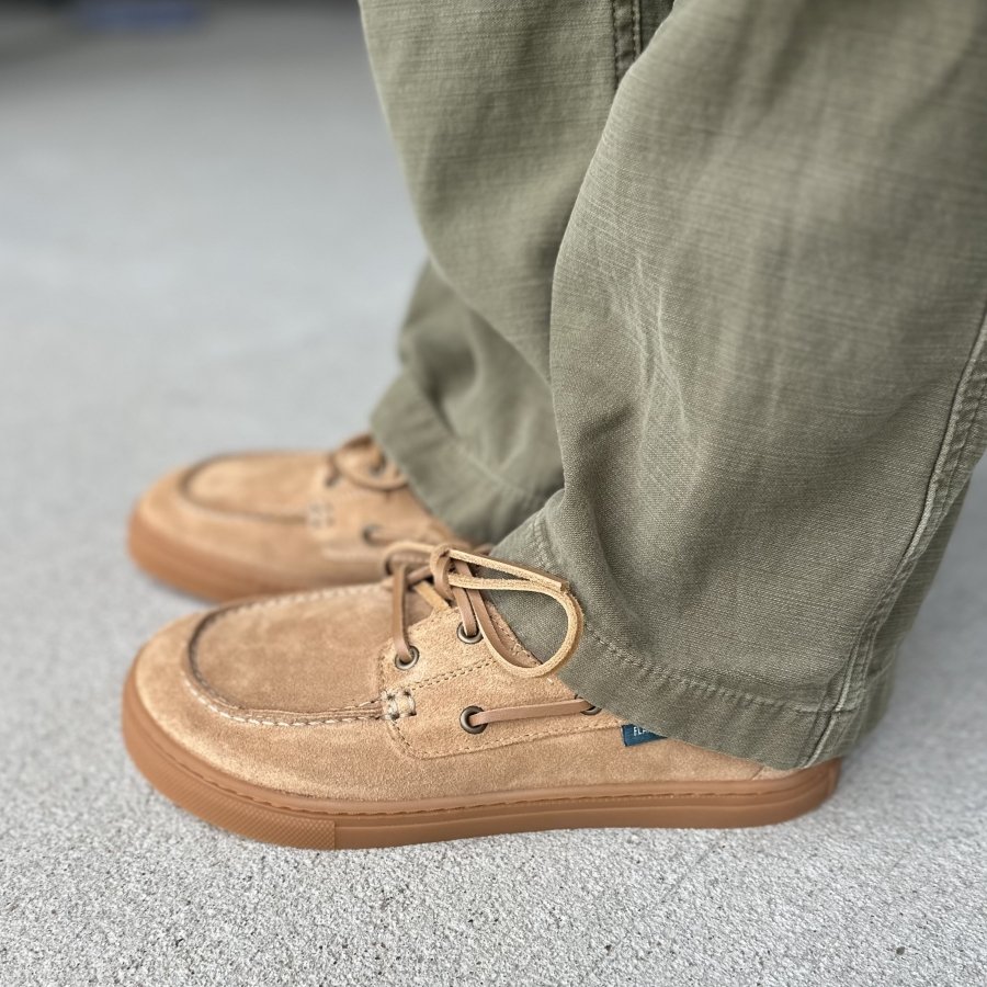 Side view of a pair of Flamingos Life Boat Shoes in tan with a flat flexible outsole, worn with green pants