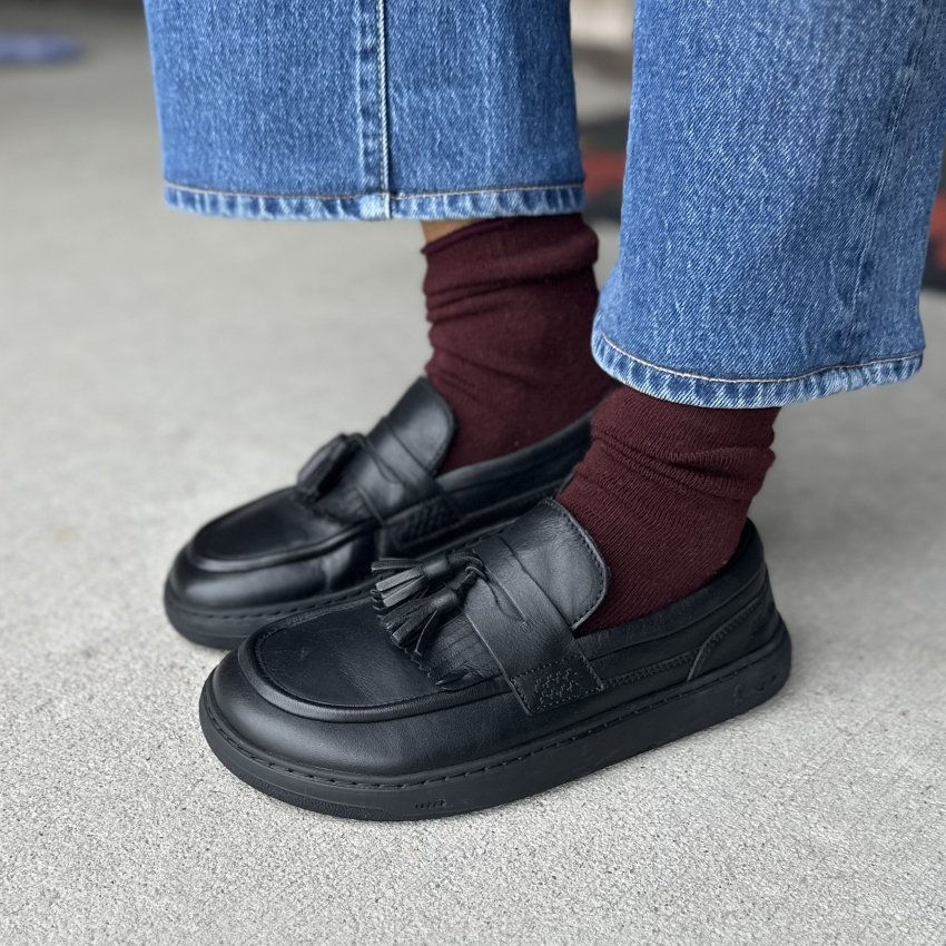 Side view of a person wearing Fleeters leather loafers with fringe and tassels, being shown with maroon socks