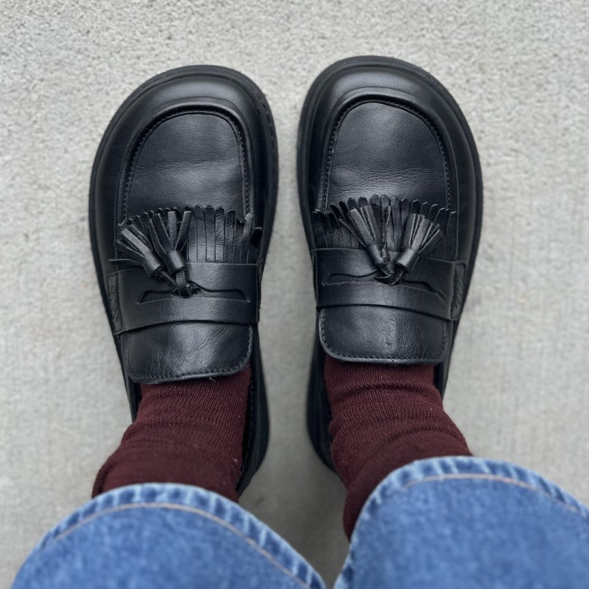 Top down view of a person in jeans, maroon scrunched socks, and wide toe box black leather loafers with fringe and tassels from Fleeters.