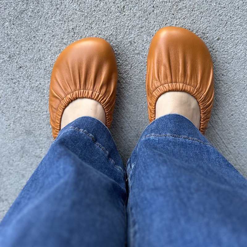 Top down view of a person's feet in ruched flats from Nugaia in an orange brown leather.