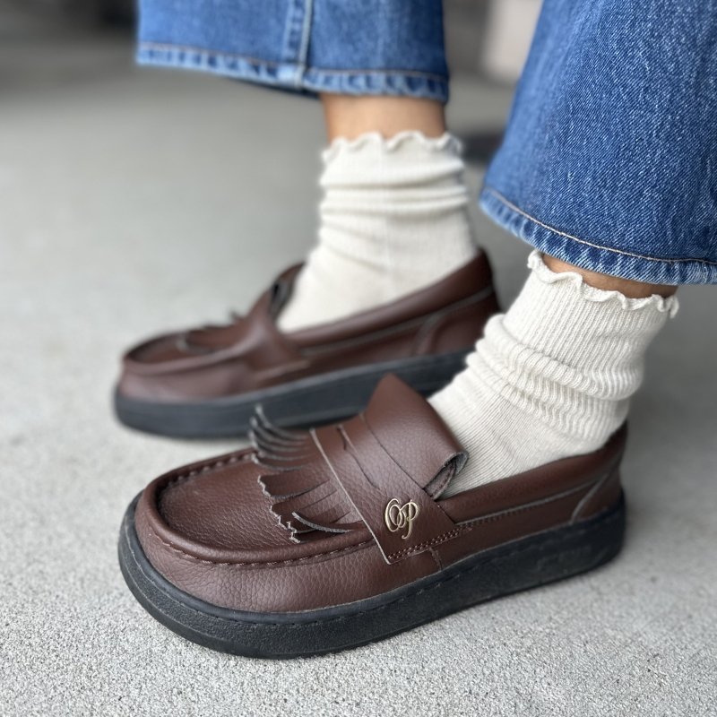 Side view of a person wearing Ohne Project brown wide toe box loafers with fringe. they're shown with ruffle socks and mid tone denim
