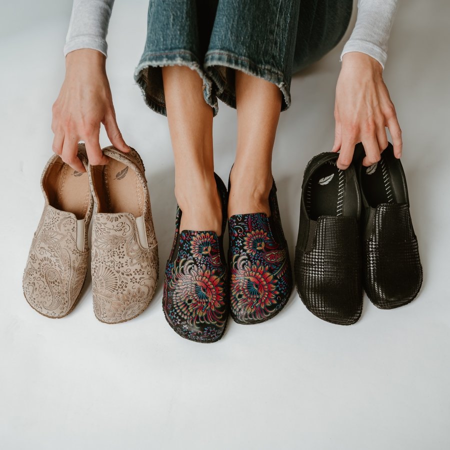 A person wearing a pair of Peerko Trim loafers with a colorful pattern and holding 2 other colors to the sides. All have a wide toe box and flat, flexible outsole.